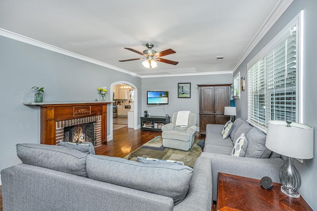 living room with crown molding, a brick fireplace, ceiling fan, and dark hardwood / wood-style flooring