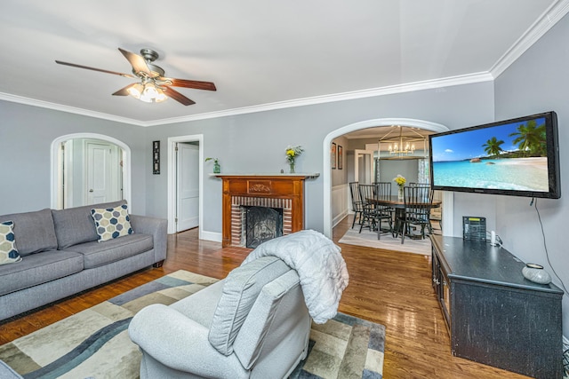 living room featuring dark wood-type flooring, ornamental molding, a fireplace, and ceiling fan with notable chandelier