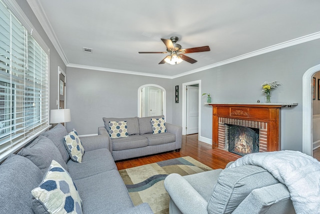 living room featuring dark wood-type flooring, crown molding, and a brick fireplace