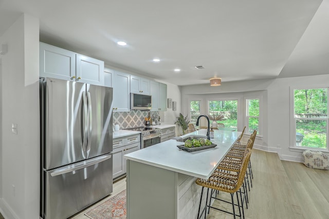 169 Southwold Cir, Goose Creek, SC 29445 - kitchen featuring appliances with stainless steel finishes, a sink, light wood finished floors, decorative backsplash, and a kitchen island with sink