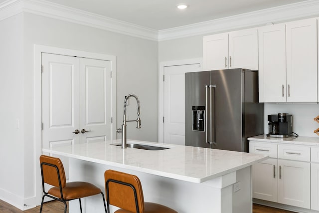 kitchen with light stone counters, ornamental molding, white cabinets, high quality fridge, and a sink