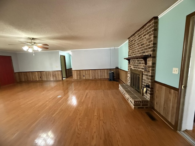 unfurnished living room with a brick fireplace, wainscoting, a textured ceiling, and wood finished floors