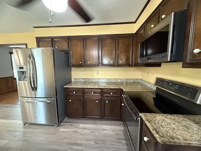 kitchen featuring appliances with stainless steel finishes, light wood-style floors, a textured ceiling, dark brown cabinets, and light stone countertops