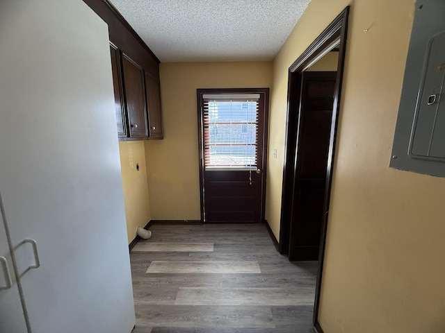 doorway to outside featuring a textured ceiling, light wood finished floors, electric panel, and baseboards