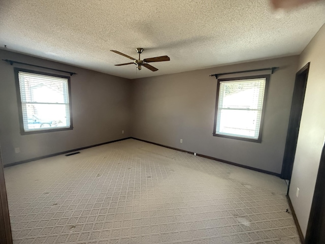 unfurnished room with ceiling fan, a textured ceiling, visible vents, and baseboards