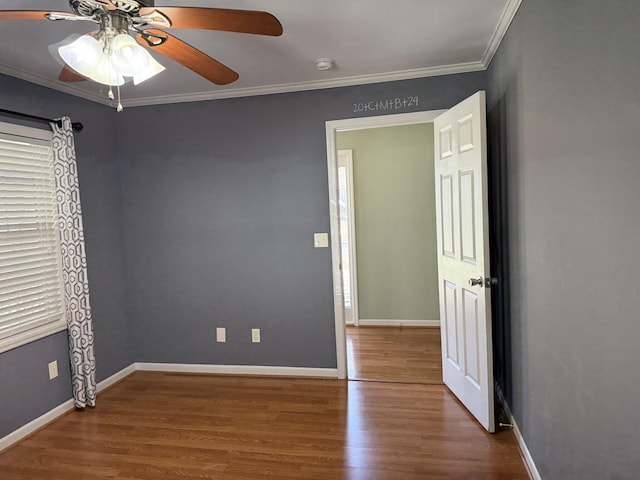 empty room featuring a ceiling fan, crown molding, baseboards, and wood finished floors