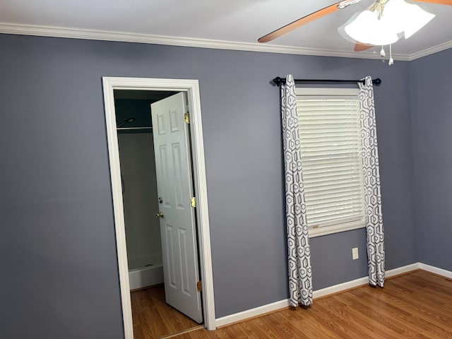 unfurnished bedroom featuring wood finished floors, a ceiling fan, baseboards, a closet, and crown molding