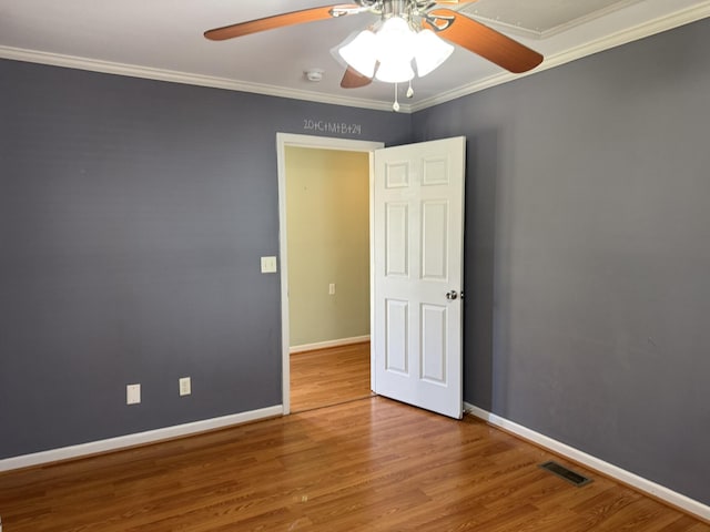 spare room with visible vents, ornamental molding, a ceiling fan, wood finished floors, and baseboards