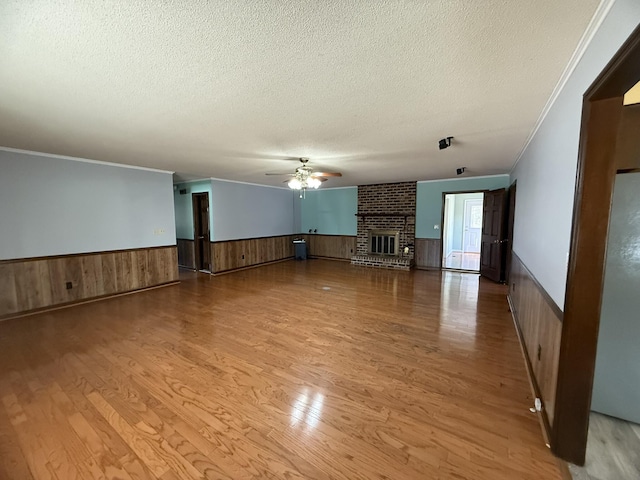 unfurnished living room with a wainscoted wall, ceiling fan, wood finished floors, a textured ceiling, and a brick fireplace