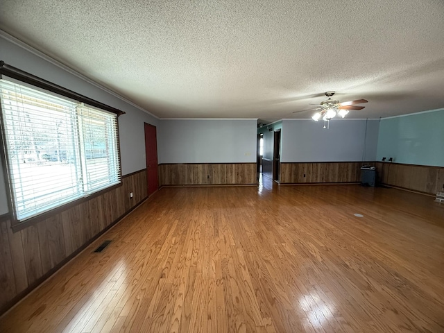 unfurnished room with light wood-style floors, a textured ceiling, and wainscoting