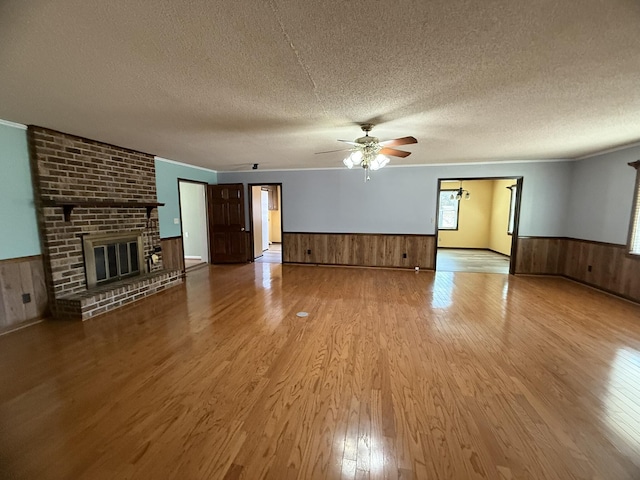 unfurnished living room featuring a textured ceiling, wainscoting, a fireplace, and light wood-style flooring