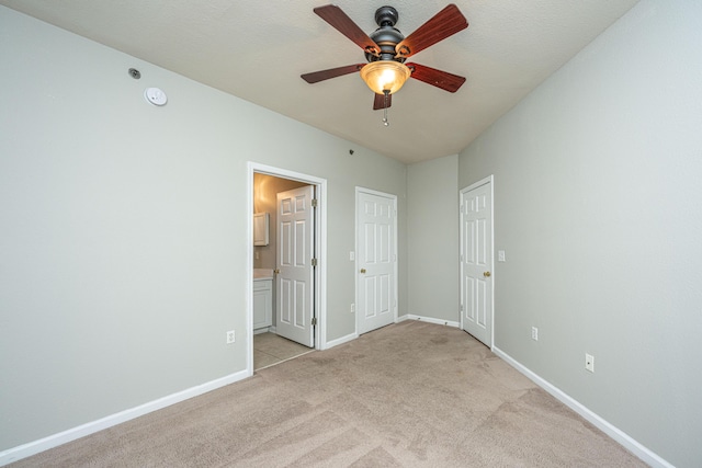 unfurnished bedroom featuring a textured ceiling, light colored carpet, ensuite bath, and ceiling fan