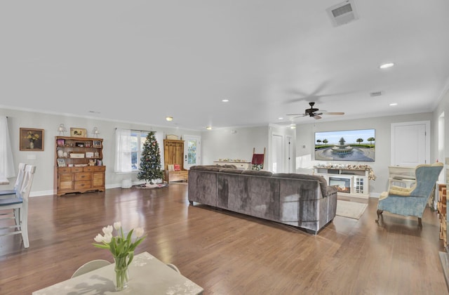 living room with dark wood-type flooring, ceiling fan, and ornamental molding