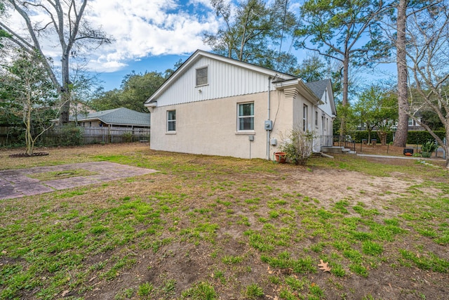 rear view of house with fence, a lawn, and stucco siding