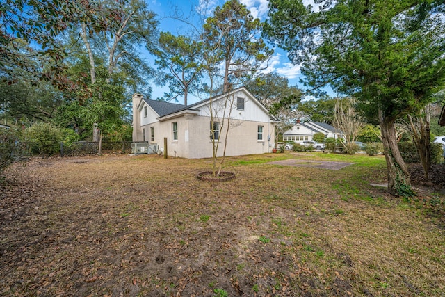 view of property exterior with stucco siding, fence, a chimney, and a lawn