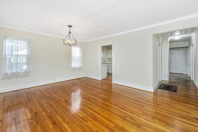 empty room featuring a notable chandelier, hardwood / wood-style floors, attic access, ornamental molding, and baseboards