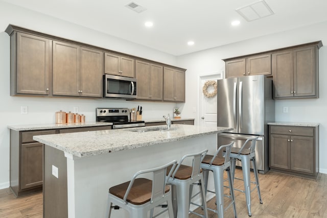 kitchen with light hardwood / wood-style floors, light stone countertops, stainless steel appliances, a kitchen bar, and a kitchen island with sink