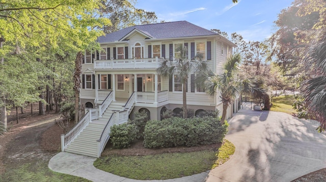 view of front facade featuring a shingled roof, covered porch, concrete driveway, stairs, and a balcony