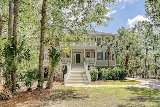 beach home featuring a front yard, a porch, stairs, and a balcony