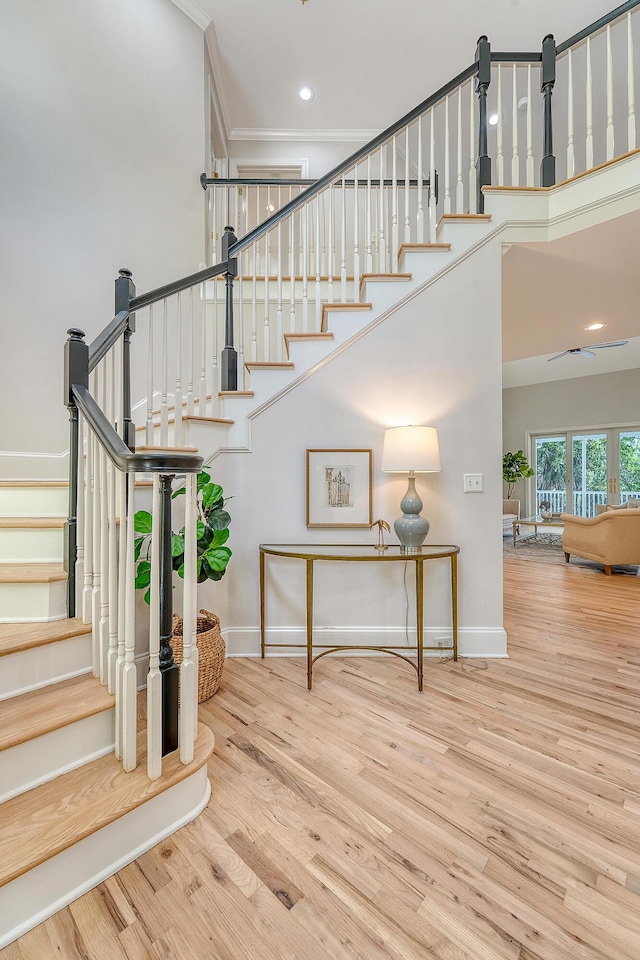 staircase with wood finished floors, a high ceiling, ornamental molding, and baseboards