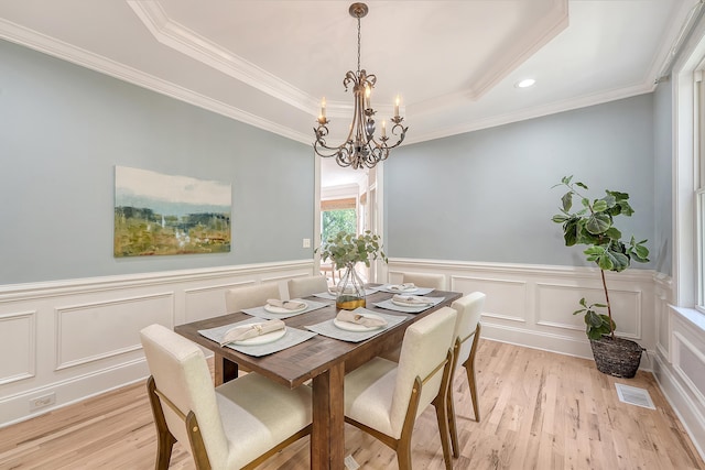 dining room featuring a decorative wall, a tray ceiling, light wood finished floors, and an inviting chandelier