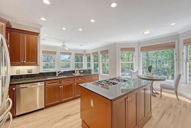 kitchen with brown cabinetry, ornamental molding, a sink, stainless steel appliances, and light wood finished floors