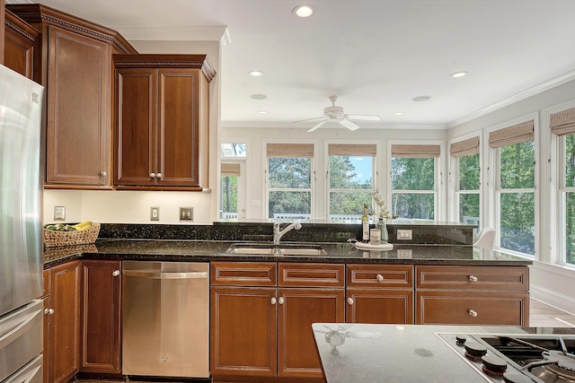 kitchen with dark stone countertops, crown molding, ceiling fan, stainless steel appliances, and a sink