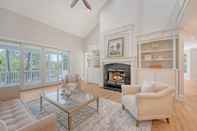 living area with light wood-type flooring, a wealth of natural light, high vaulted ceiling, and a high end fireplace