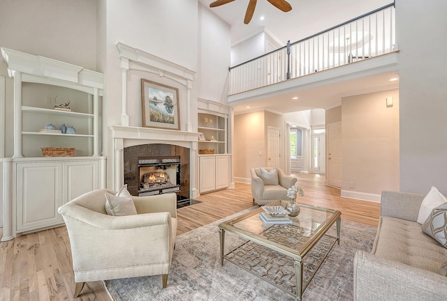 living area with built in features, a high ceiling, a ceiling fan, a fireplace, and wood finished floors
