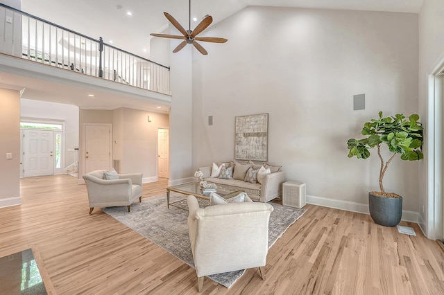 living area featuring baseboards, light wood-type flooring, a high ceiling, and a ceiling fan