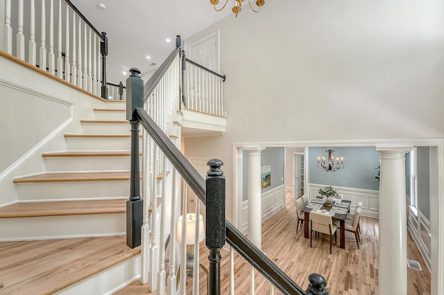 stairway featuring an inviting chandelier, crown molding, a wainscoted wall, a decorative wall, and wood finished floors