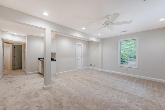 below grade area with visible vents, light colored carpet, baseboards, and ceiling fan