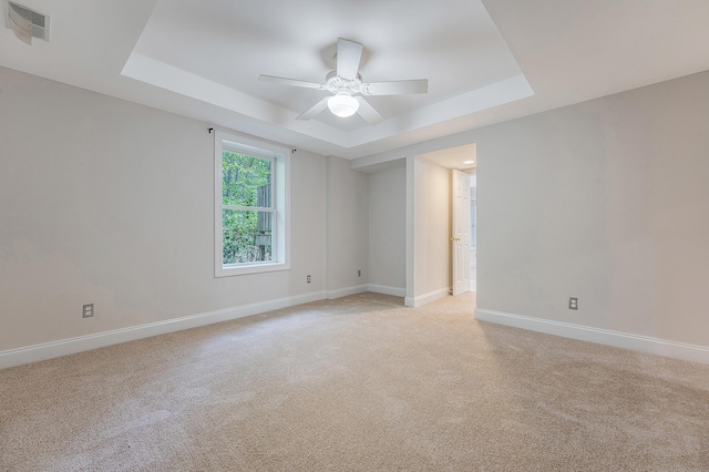 spare room featuring a tray ceiling, baseboards, light colored carpet, and visible vents