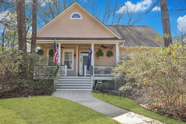 view of front facade with a front yard, covered porch, roof with shingles, and ceiling fan