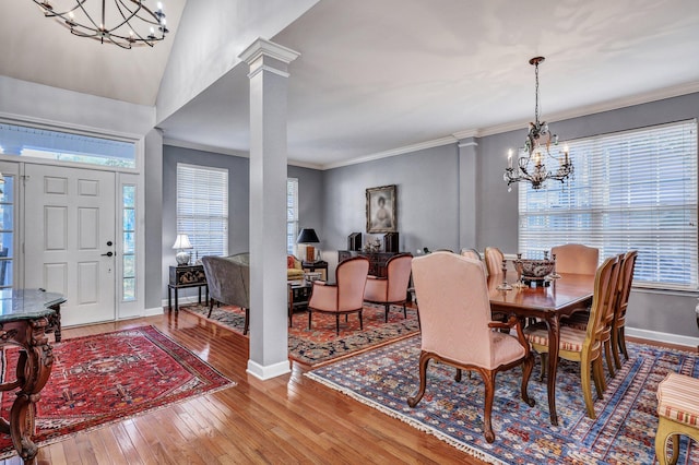 dining area with baseboards, ornamental molding, wood-type flooring, decorative columns, and an inviting chandelier