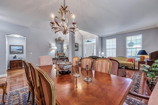 dining area featuring arched walkways, a notable chandelier, baseboards, vaulted ceiling, and light wood finished floors