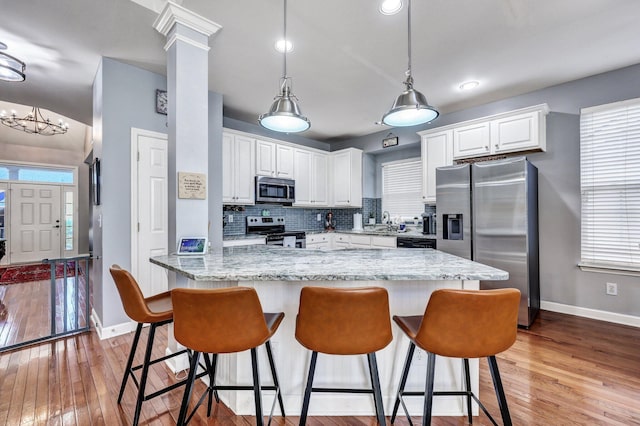 kitchen featuring decorative backsplash, light wood-style flooring, appliances with stainless steel finishes, a kitchen breakfast bar, and white cabinetry