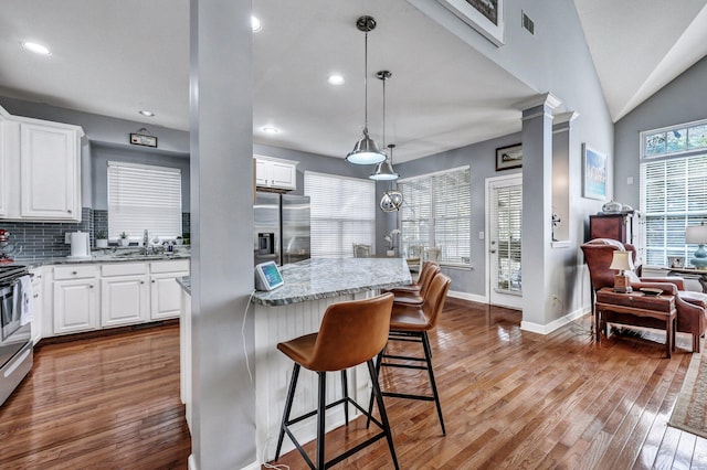 kitchen with light stone counters, dark wood finished floors, a sink, stainless steel fridge, and ornate columns