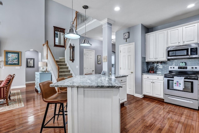 kitchen with arched walkways, decorative columns, stainless steel appliances, decorative backsplash, and white cabinetry