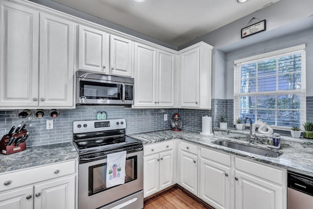 kitchen featuring stainless steel appliances, tasteful backsplash, light wood-style floors, white cabinets, and a sink