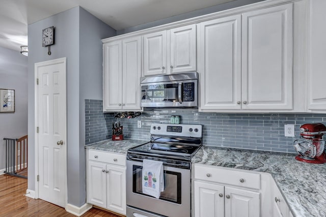 kitchen with baseboards, white cabinets, decorative backsplash, light wood-style flooring, and appliances with stainless steel finishes