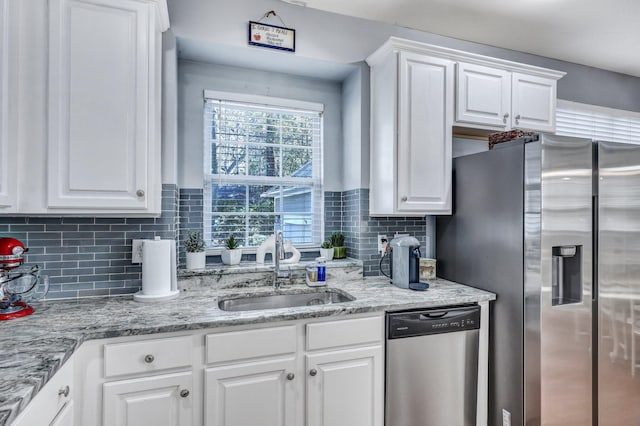 kitchen featuring white cabinets, appliances with stainless steel finishes, a sink, light stone countertops, and backsplash