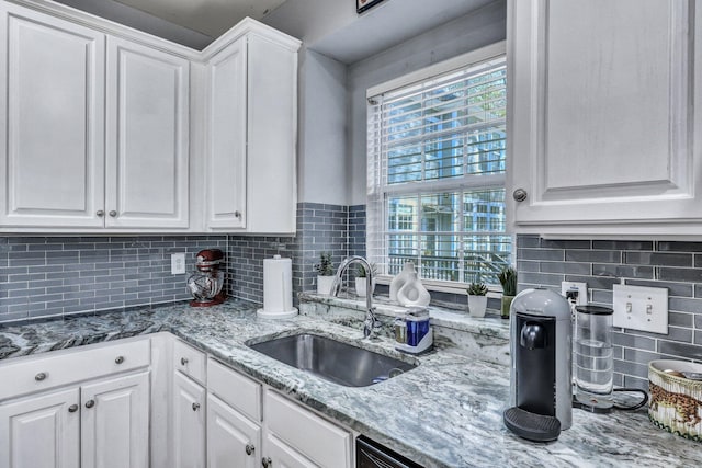 kitchen with light stone counters, white cabinetry, backsplash, and a sink