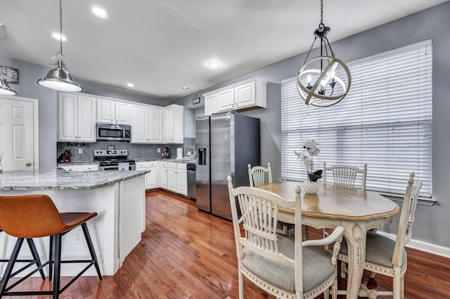 kitchen featuring tasteful backsplash, white cabinets, light wood-style flooring, appliances with stainless steel finishes, and light stone countertops