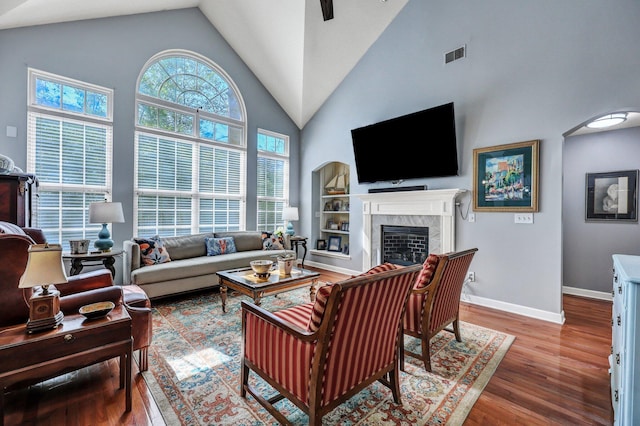 living area with baseboards, visible vents, wood finished floors, a fireplace, and high vaulted ceiling