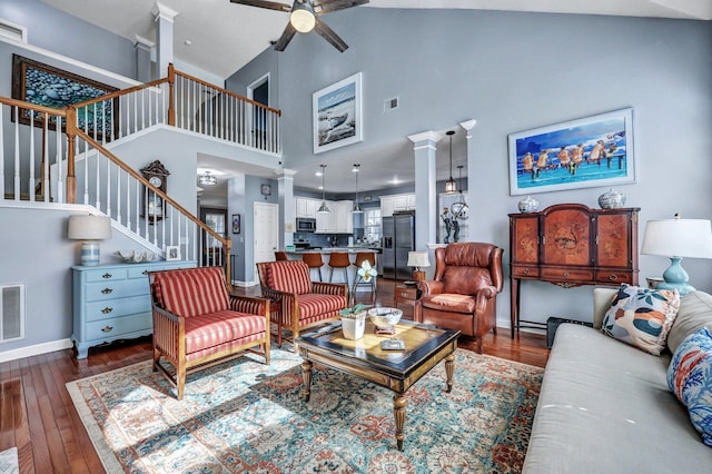 living area with ornate columns, visible vents, dark wood-type flooring, baseboards, and stairs