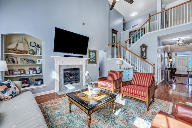 living area with baseboards, a towering ceiling, wood finished floors, stairs, and a fireplace