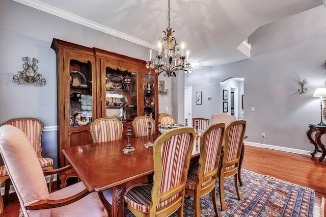 dining space featuring baseboards, crown molding, arched walkways, and wood finished floors