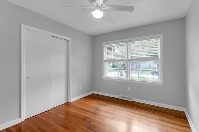 unfurnished bedroom featuring a closet, baseboards, visible vents, ceiling fan, and wood finished floors