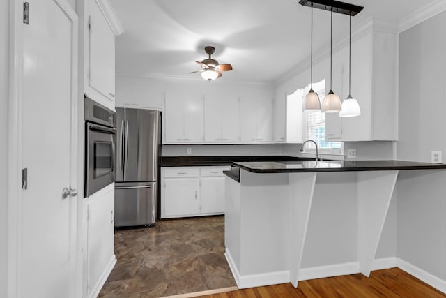 kitchen with ornamental molding, dark countertops, a peninsula, white cabinetry, and stainless steel appliances